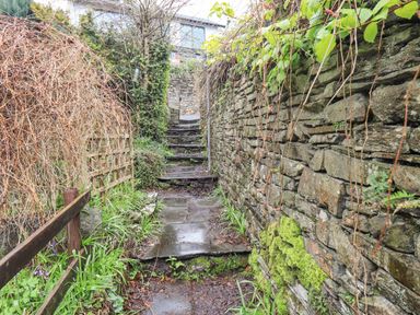 A stone pathway with steps between stone walls and greenery at Hideaway Cottage in Ambleside
