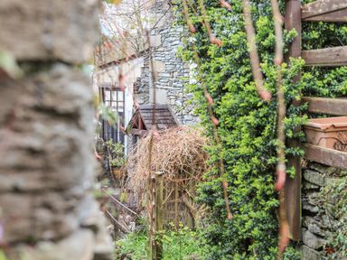 An outdoor garden area with a stone wall wooden fence green shrubs and a building with a stone exterior at Hideaway Cottage in Ambleside