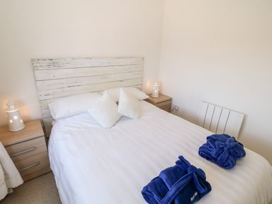 A bedroom with a double bed with white bedding and pillows two bedside tables with lamps and folded blue robes at Bryn Mor in Church Bay