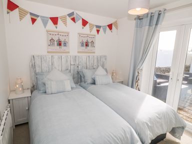 A bedroom with two single beds with light blue bedding and rustic headboard at Bryn Mor in Church Bay