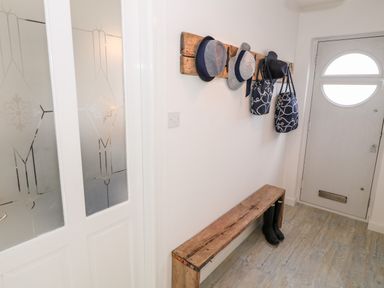 An entryway with a wooden bench black boots under it hats and bags hanging on a wooden wall rack at Bryn Mor in Church Bay