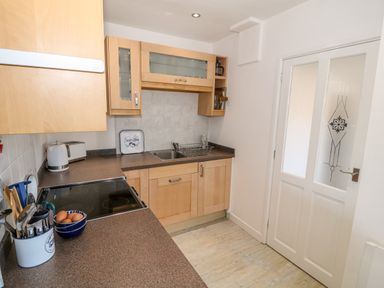 A kitchen with wooden cabinets a ceramic stovetop utensils in a container a bowl of eggs and a white door with frosted glass at Bryn Mor in Church Bay