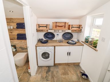 A utility room with washing machine countertop baskets plates and bowls at Bryn Mor in Church Bay