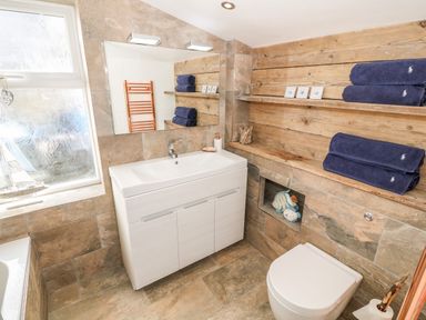 A bathroom with a sink cabinet a toilet blue towels on wooden shelves and a frosted window at Bryn Mor in Church Bay
