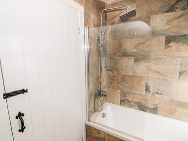 A bathroom with a bathtub and a showerhead attached to a tiled wall at Bryn Mor in Church Bay