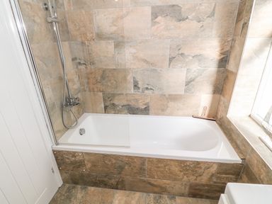 A bathroom with a bathtub and a showerhead attached to the wall with tile surrounding the tub at Bryn Mor in Church Bay
