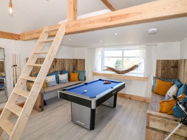 A game room with a pool table a wooden ladder wooden bench seating with cushions and a window with a wooden decor piece at Bryn Mor in Church Bay