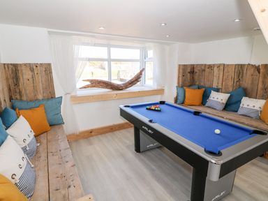 A game room with a blue pool table and wooden benches with cushions by a window at Bryn Mor in Church Bay