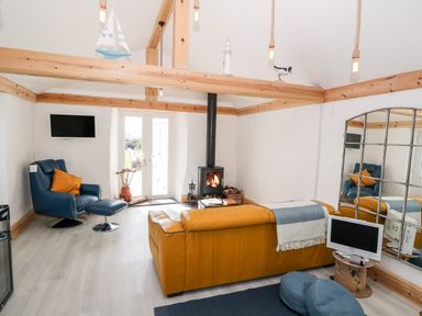 A living room with a yellow sofa a blue armchair a wood burning stove and a large wall mirror at Bryn Mor in Church Bay
