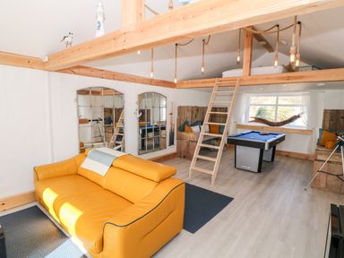 A game room with a yellow sofa a pool table a loft bed with wooden ladder and built in wooden benches at Bryn Mor in Church Bay