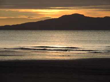 A beach with gentle waves and a large mountain in the background at sunset