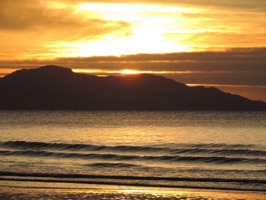A sunset over the sea with mountains in the background and small waves in the foreground at Bryn Mor in Church Bay