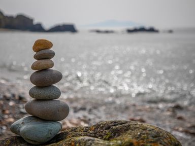 A stack of seven balanced stones on a rocky shore with the sea and distant land in the background