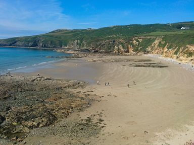 A sandy beach with rocky areas and people walking near cliffs and hills at Bryn Mor in Church Bay