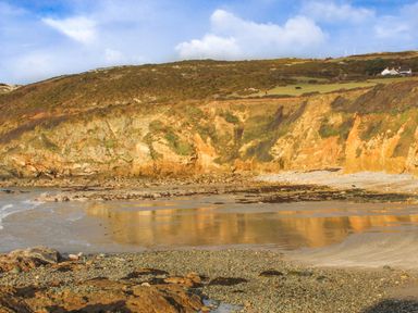 A rocky beach with cliffs and grassy hills under a blue sky at Bryn Mor in Church Bay