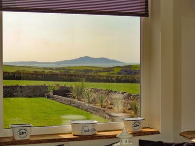 A window overlooking a green garden with stone walls and plants with hills and sea in the background at Bryn Mor in Church Bay