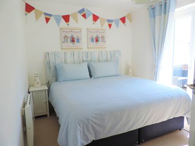 A bedroom with a double bed light blue bedding bedside tables with lamps a window with curtains and wall decorations at Bryn Mor in Church Bay