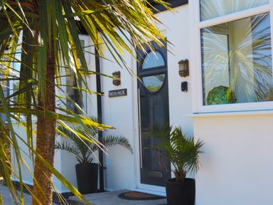 The front entrance of a house with a dark door two potted plants and a window with a decorative object inside at Bryn Mor in Church Bay