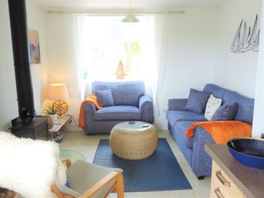A living room with two blue sofas a wicker coffee table a black stove and a wooden armchair with a white fur throw at Bryn Mor in Church Bay