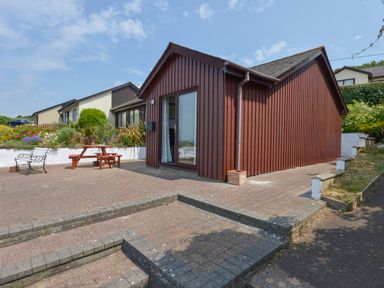 A brown wooden cottage with a patio table and bench seating outside at SoundView in Down Thomas