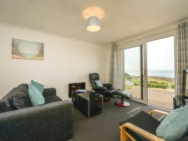 A living room with a sofa armchair recliner glass coffee table and sliding doors opening to a sea view at SoundView in Down Thomas