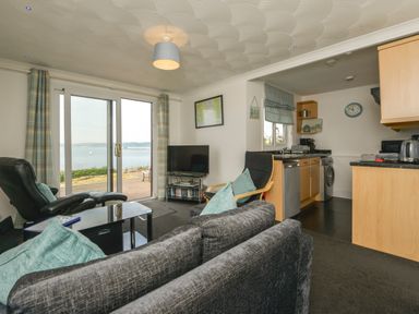 A living room with sofas chairs a television and sliding glass doors leading to a garden and sea view at SoundView in Down Thomas