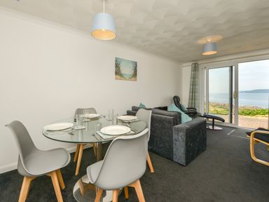 A dining area with a round glass table and four chairs next to a living room with sofas and a sliding glass door overlooking a sea view at SoundView in Down Thomas
