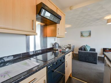 A kitchen with black countertop and light wood cabinets next to a dining table and gray sofa at SoundView in Down Thomas