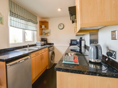 A kitchen with wooden cabinets a sink a washing machine a microwave a kettle and a window at SoundView in Down Thomas