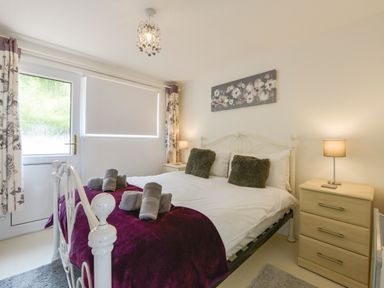 A bedroom with a white metal bed frame purple blanket rolled towels bedside tables with lamps and floral curtains at SoundView in Down Thomas