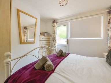 A bedroom with a bed having rolled towels on a purple throw near a window with blinds and a door at SoundView in Down Thomas