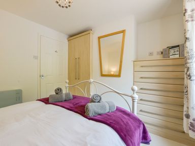 A bedroom with a bed covered in white bedding and purple blanket towels rolled on the bed wooden wardrobe and chest of drawers with a mirror on the wall at SoundView in Down Thomas