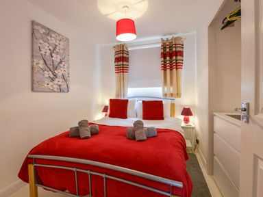 A bedroom with a bed covered in a red blanket and two red pillows with rolled towels on top at SoundView in Down Thomas