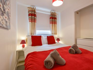 A bedroom with a double bed red pillows and red blanket two bedside tables with red lamps and a window with curtains at SoundView in Down Thomas