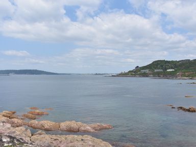A coastal scene with rocky shore in the foreground and hills with buildings in the background at SoundView in Down Thomas