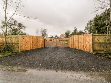 A gravel driveway leading to a wooden double gate surrounded by wooden fences with trees and a building in the background at Halmore Pod Halmore near Berkeley