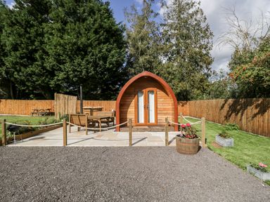 A wooden pod with a patio area and outdoor seating in a fenced garden at Halmore Pod in Halmore near Berkeley