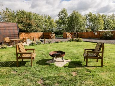 A grassy outdoor area with two wooden chairs around a fire pit and a wooden building in the background at Halmore Pod Halmore near Berkeley
