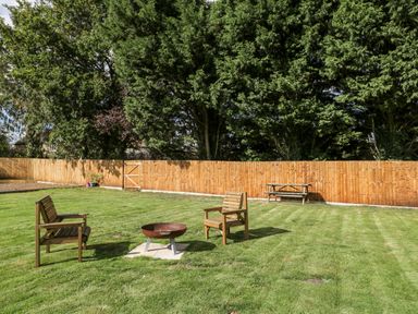 A backyard with two wooden chairs around a fire pit and a wooden picnic table near a wooden fence at Halmore Pod in Halmore near Berkeley
