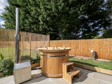 An outdoor wooden hot tub with steps next to a stainless steel heater surrounded by a grass lawn and wooden fencing at Halmore Pod in Halmore near Berkeley