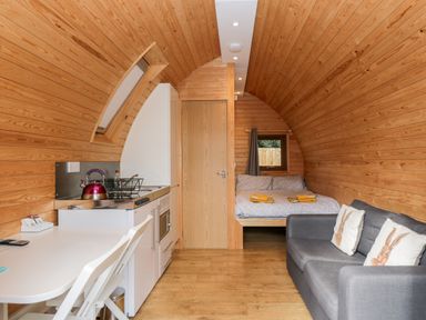 An interior of a wooden pod with a small kitchen area dining table bed and sofa at Halmore Pod in Halmore near Berkeley
