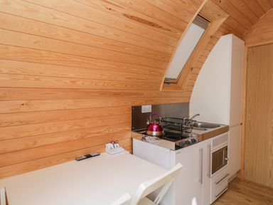 A small kitchen with a white table and chair a stove with a kettle a dish rack a sink and a wooden wall at Halmore Pod Halmore near Berkeley
