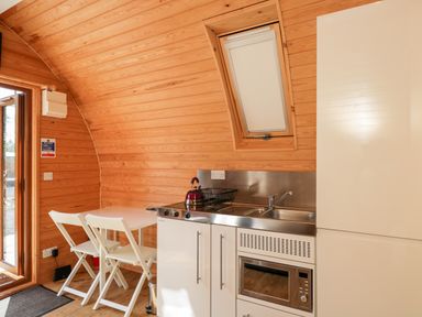 A kitchen area with white cabinets a microwave a sink a small table and two chairs in a wooden pod at Halmore Pod Halmore near Berkeley