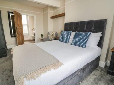 A bedroom with a double bed with blue pillows and a beige blanket next to a wooden door at Through The Porthole in Falmouth