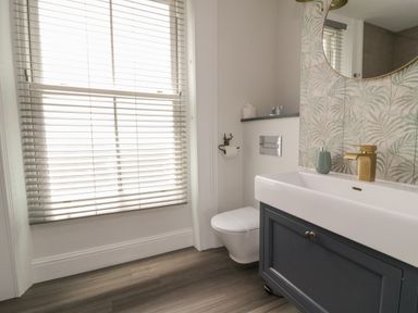 A bathroom with a window with blinds a toilet a sink with gold faucet and a mirror at Through The Porthole in Falmouth