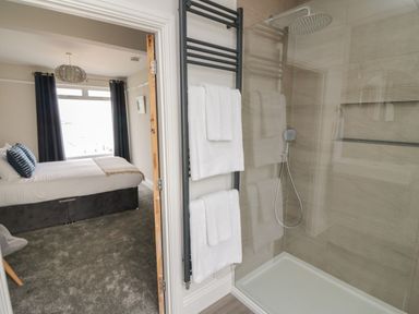 A bathroom with a glass shower and white towels on a rack adjoining a bedroom with a bed and window at Through The Porthole in Falmouth