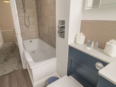 A bathroom with a bathtub shower combination and toiletries on a countertop at Through The Porthole in Falmouth