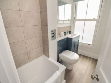 A bathroom with a bathtub a toilet and a sink with blue cabinets at Through The Porthole in Falmouth