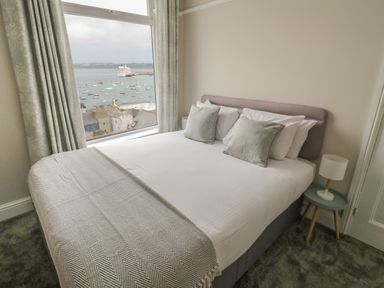 A bedroom with a bed and pillows next to a window overlooking boats at Through The Porthole in Falmouth