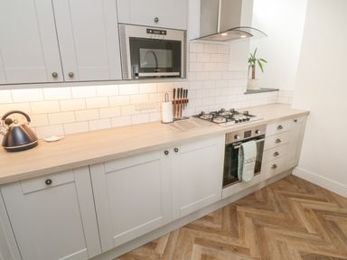 A kitchen with white cabinets a wooden countertop a microwave a gas stove an oven a kettle and a plant at Through The Porthole in Falmouth